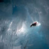 A climber is seen from below through a small opening in a mass of ice.